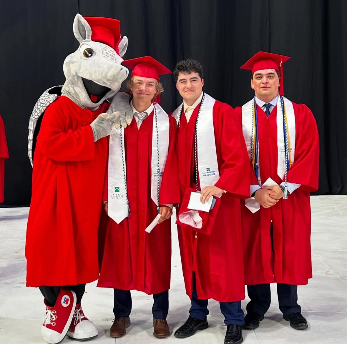 Brian in red graduation regalia with the San Antonio College mascot