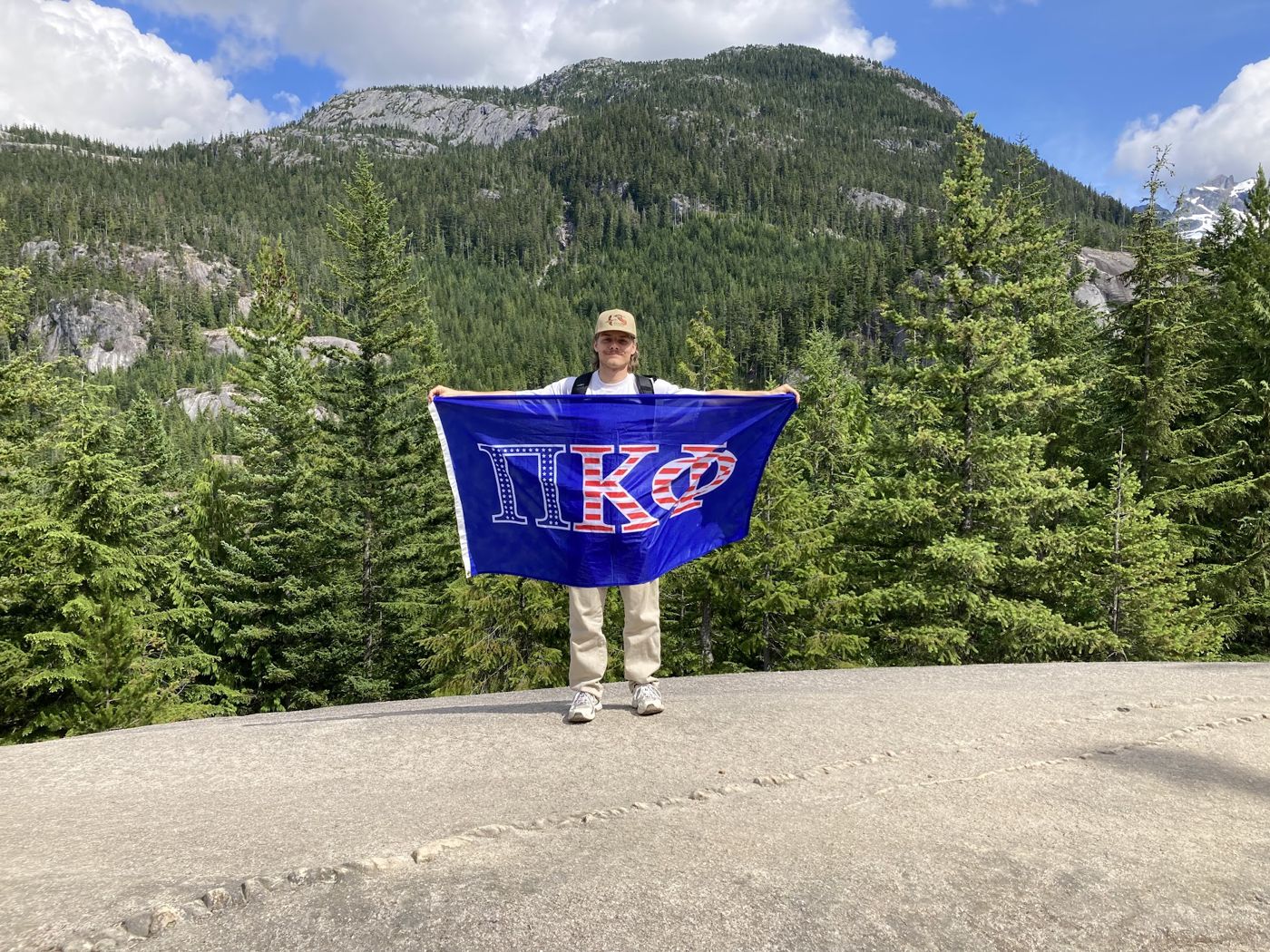 Brian holding a Pi Kappa Phi flag on a rocky summit in the Canadian mountains